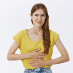 Girl regret eating food near subway. Portrait of displeased worried woman feeling discomfort in stomach holding hands on belly smirking and frowning looking left having stomachache or disorder