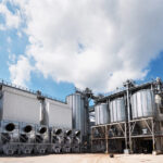 Agricultural Silos. Building Exterior. Storage and drying of grains, wheat, corn, soy, sunflower against the blue sky with white clouds