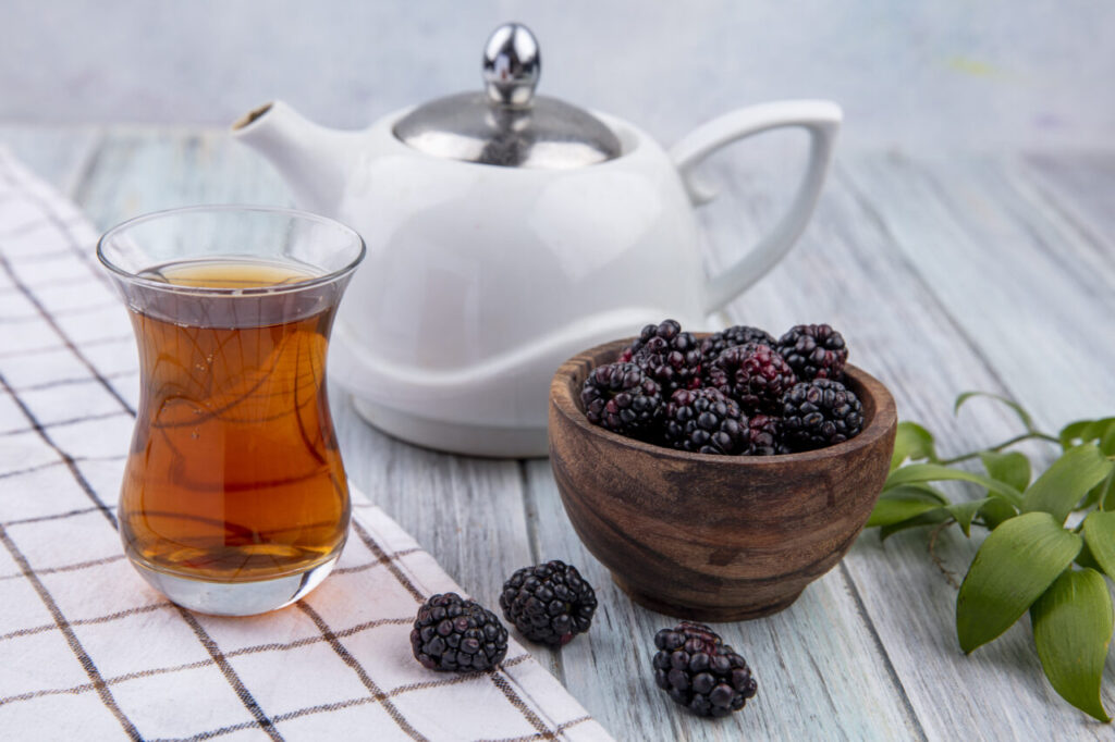 front view armudu glass of tea with teapot and blackberry on a gray background