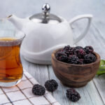 front view armudu glass of tea with teapot and blackberry on a gray background