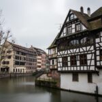 River surrounded by colorful buildings and greenery under a cloudy sky in Strasbourg in France