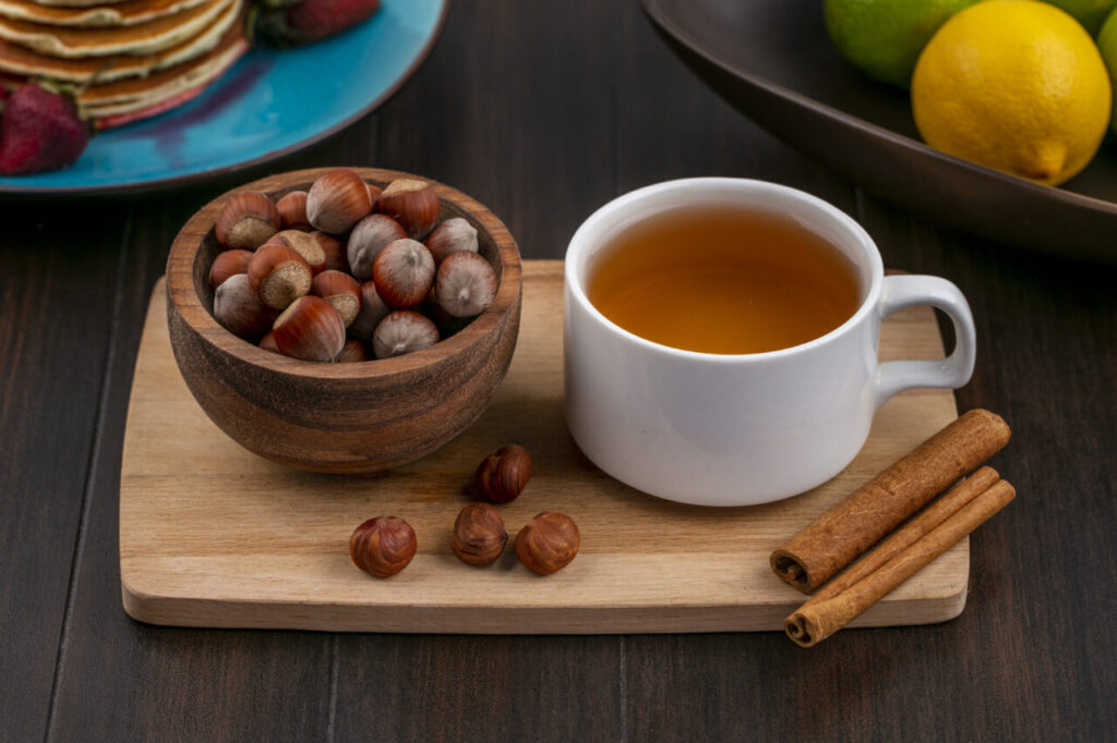 front view hazelnut in a bowl with a cup of tea and cinnamon on a board on a wooden background